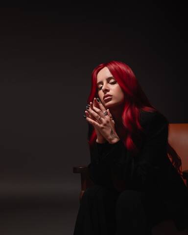 CERES sitting in a chair with her eyes closed and hands clasped, captured in a soft, introspective editorial moment.