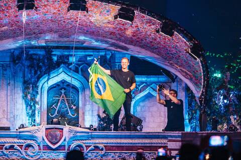 Armin van Buuren performing on the Tomorrowland Brasil 2025 mainstage, holding the Brazilian flag as the crowd celebrates under confetti.
