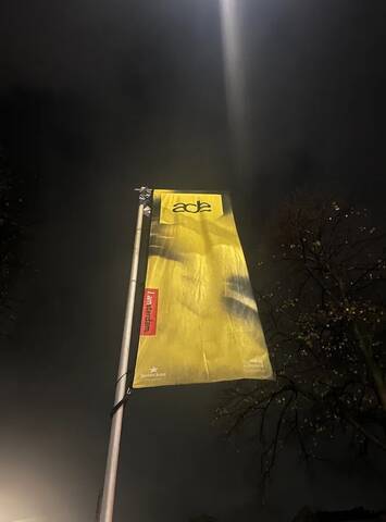Amsterdam Dance Event 2025 flag illuminated at night in Amsterdam, featuring the ADE logo and city branding