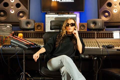 Stephanie B sitting in a music studio, surrounded by mixing equipment and soundboards, focused and ready to create her next track.