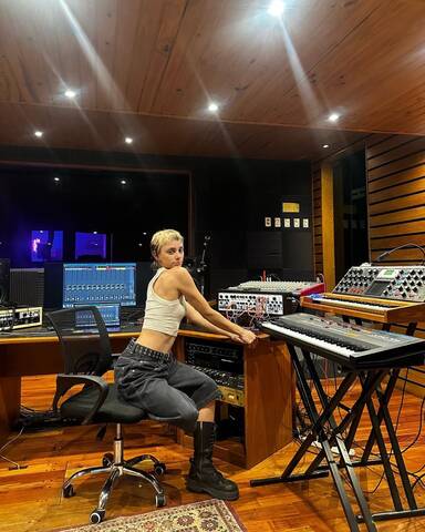  Ludmila Di Pasquale, DJ and music producer, inside a professional recording studio, surrounded by analog synthesizers, mixing desk and keyboards during a studio session.