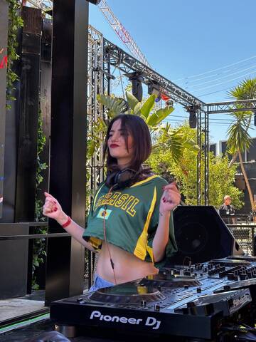 Lorena Fabbrini performing in a Brazil national team shirt during her DJ set, representing her roots on an international stage.
